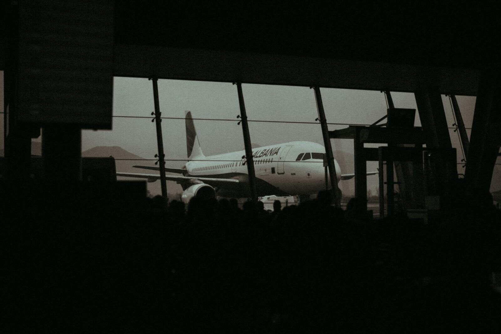 Silhouette of an airplane and waiting passengers inside an airport terminal at dusk.