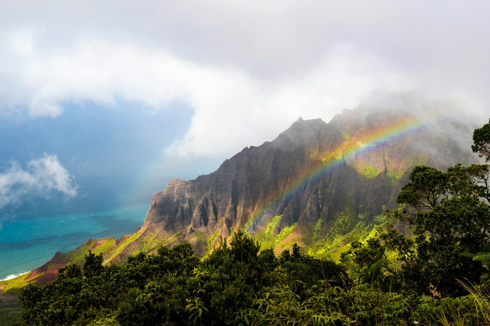 A vivid rainbow arcing over the lush green mountains of Kauai Hawaii — the Garden Isle earns its nickname year-round