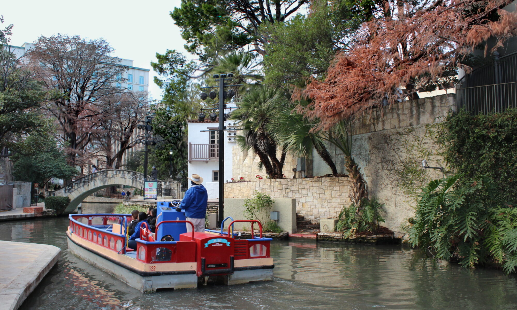 The San Antonio River Walk lined with cypress trees, restaurants, and stone footpaths below downtown