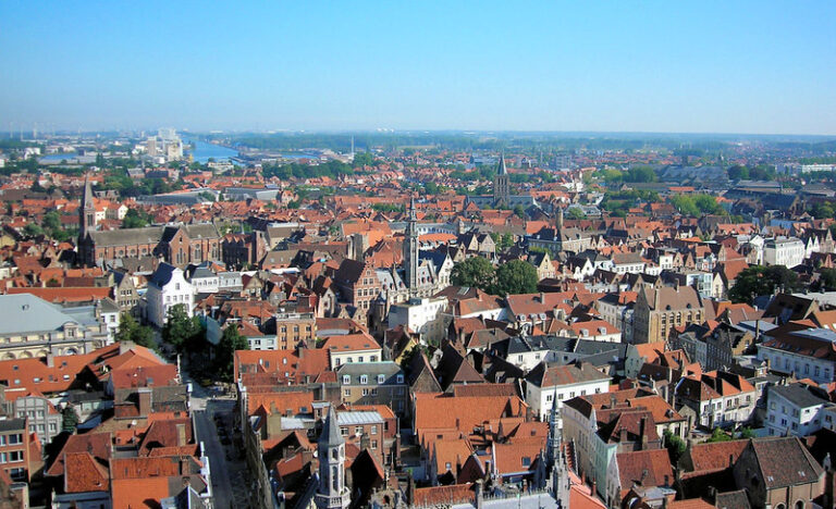 Aerial view of Bruges red rooftops and church towers under a blue sky