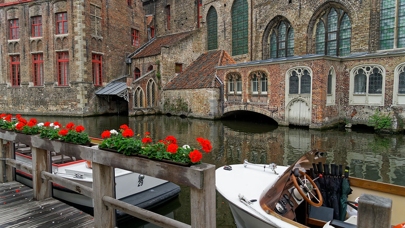 Flower-lined canal in Bruges with a tour boat and medieval houses