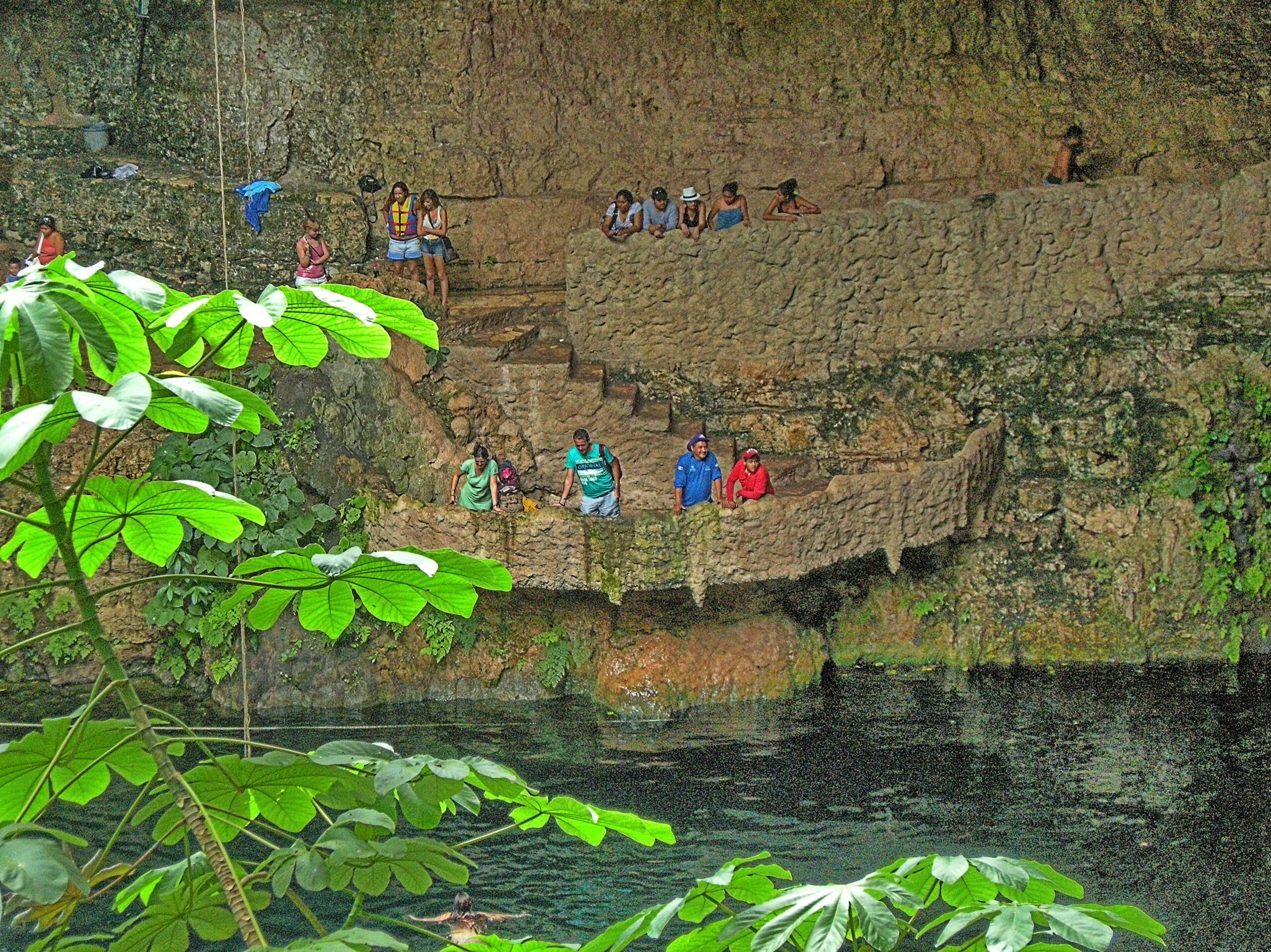 Turquoise water in an open cenote surrounded by rock and greenery in Yucatan Mexico