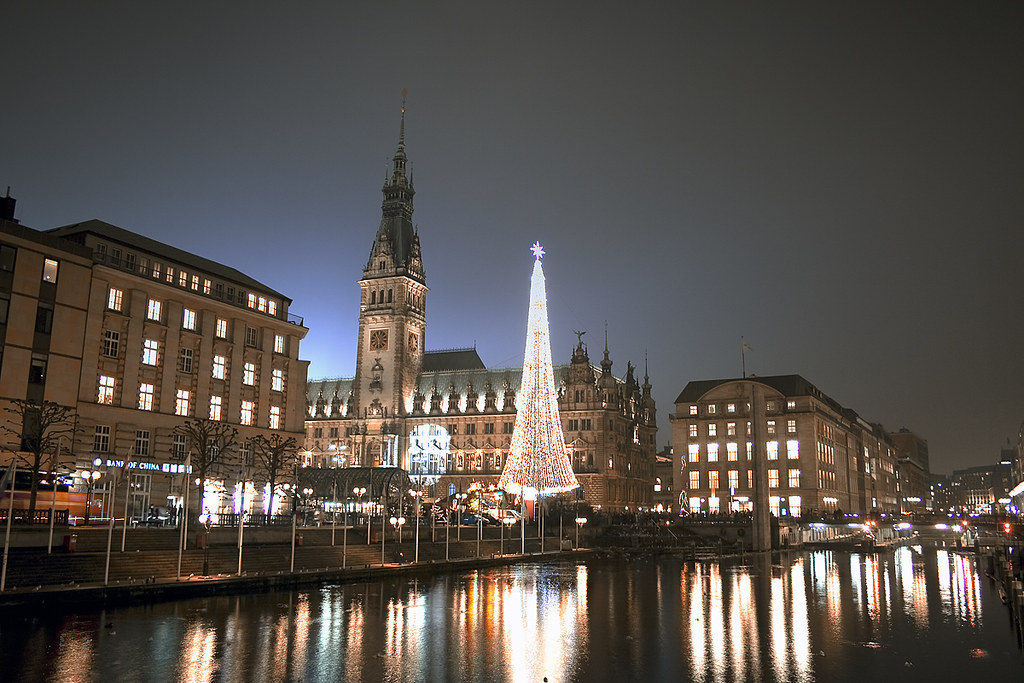 Illuminated Christmas market with a lit tree reflected in the water at night