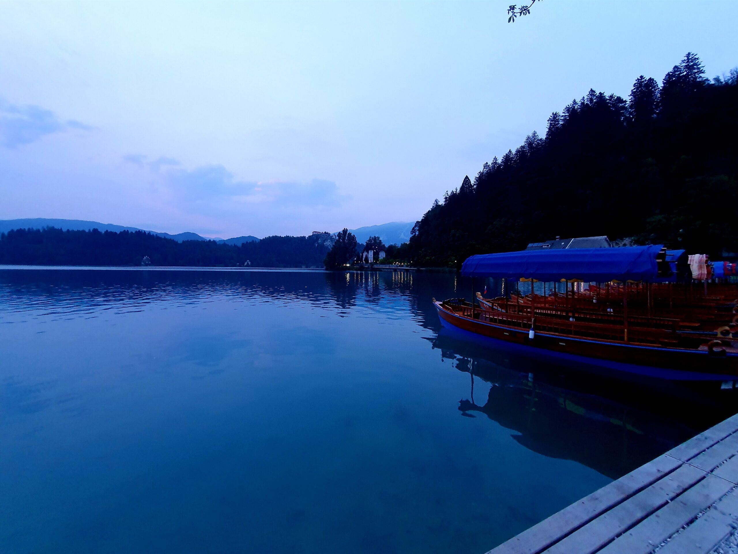 Wooden pletna boats on the turquoise water of Lake Bled with Bled Castle on the cliff above