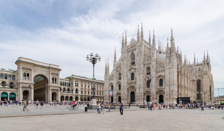 The white marble Gothic facade of the Duomo di Milano against a blue sky