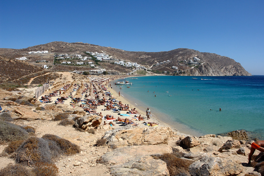 Sun loungers on a Mykonos beach beside turquoise Aegean water