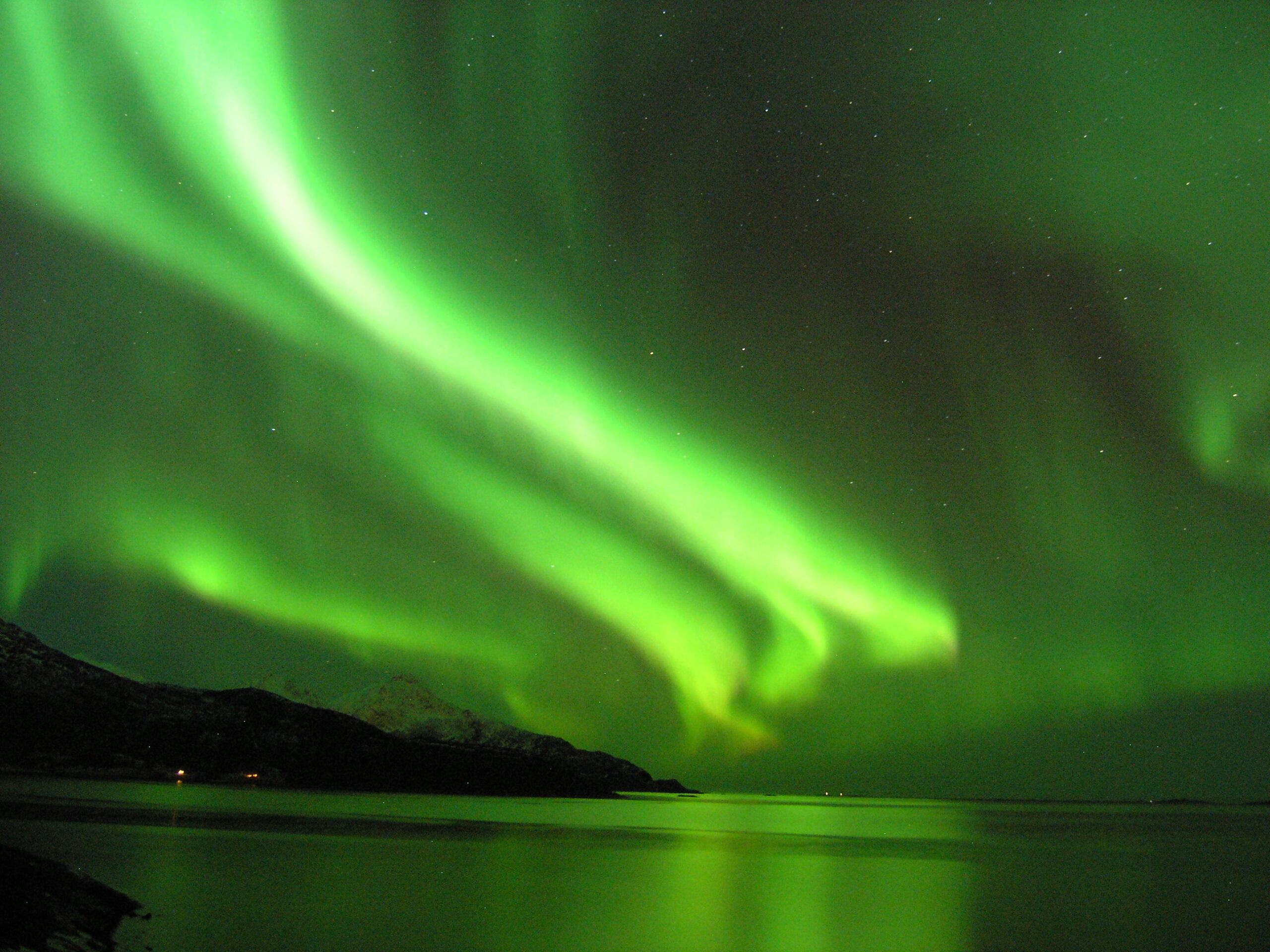 Green northern lights arcing over snow covered hills near Tromso Norway