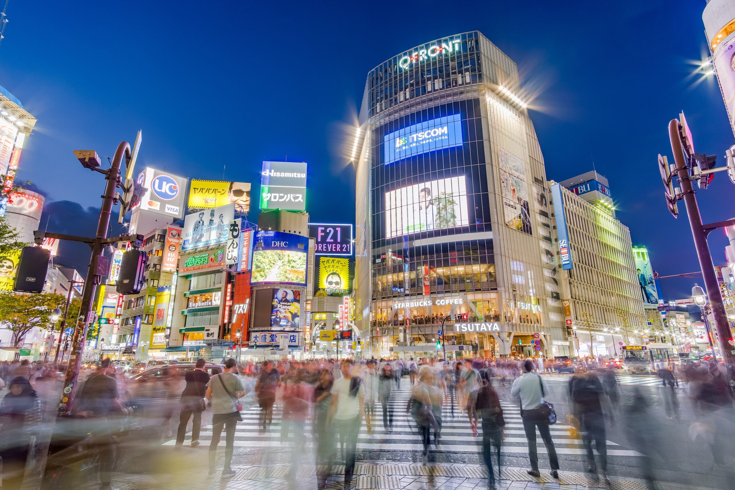 Crowds crossing the busy Shibuya Scramble Crossing surrounded by bright screens in Tokyo