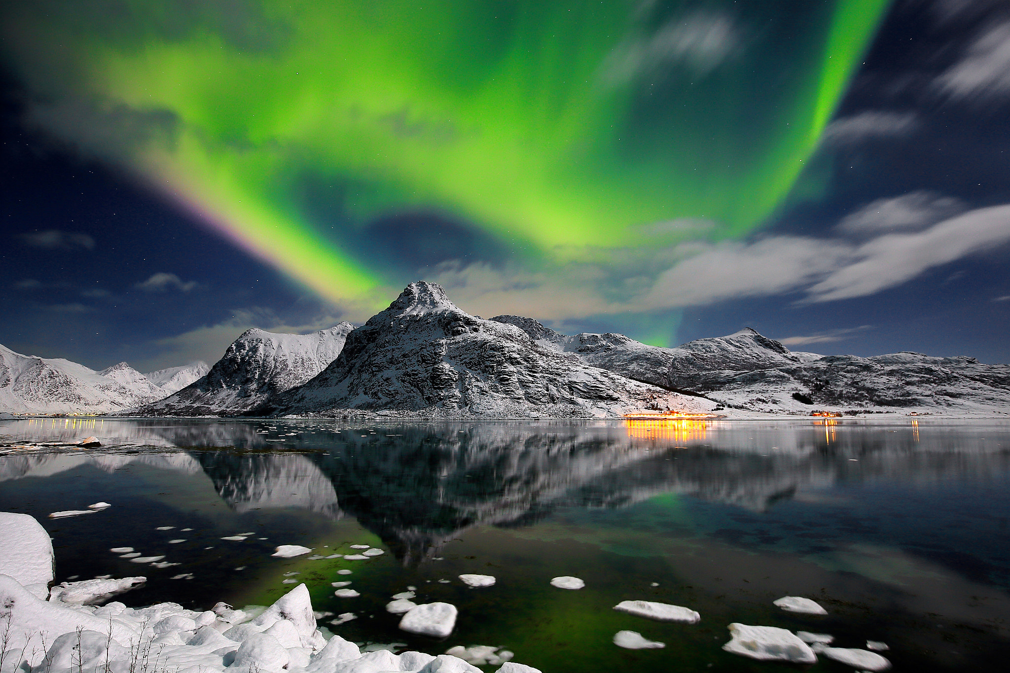 Green northern lights swirling over a snowy Scandinavian landscape at night