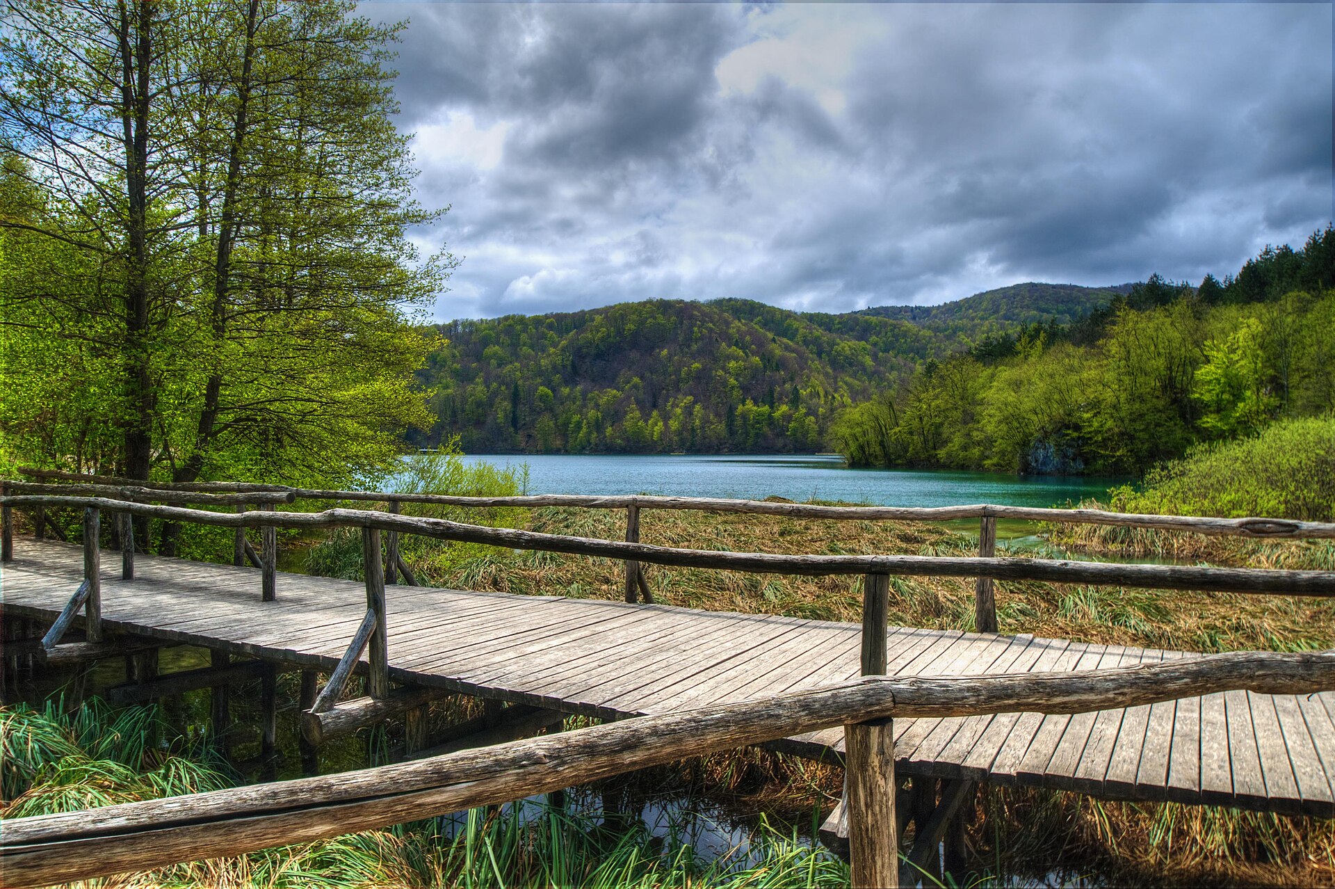 Wooden boardwalk trail running alongside a lake and forested hills at Plitvice Lakes