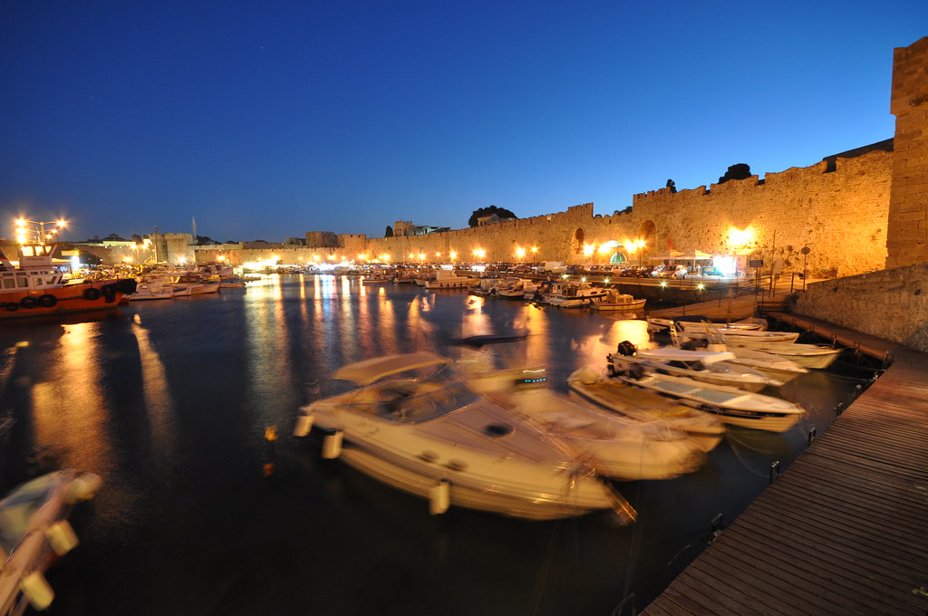 Floodlit medieval walls of Rhodes Town reflected in the harbour after dark