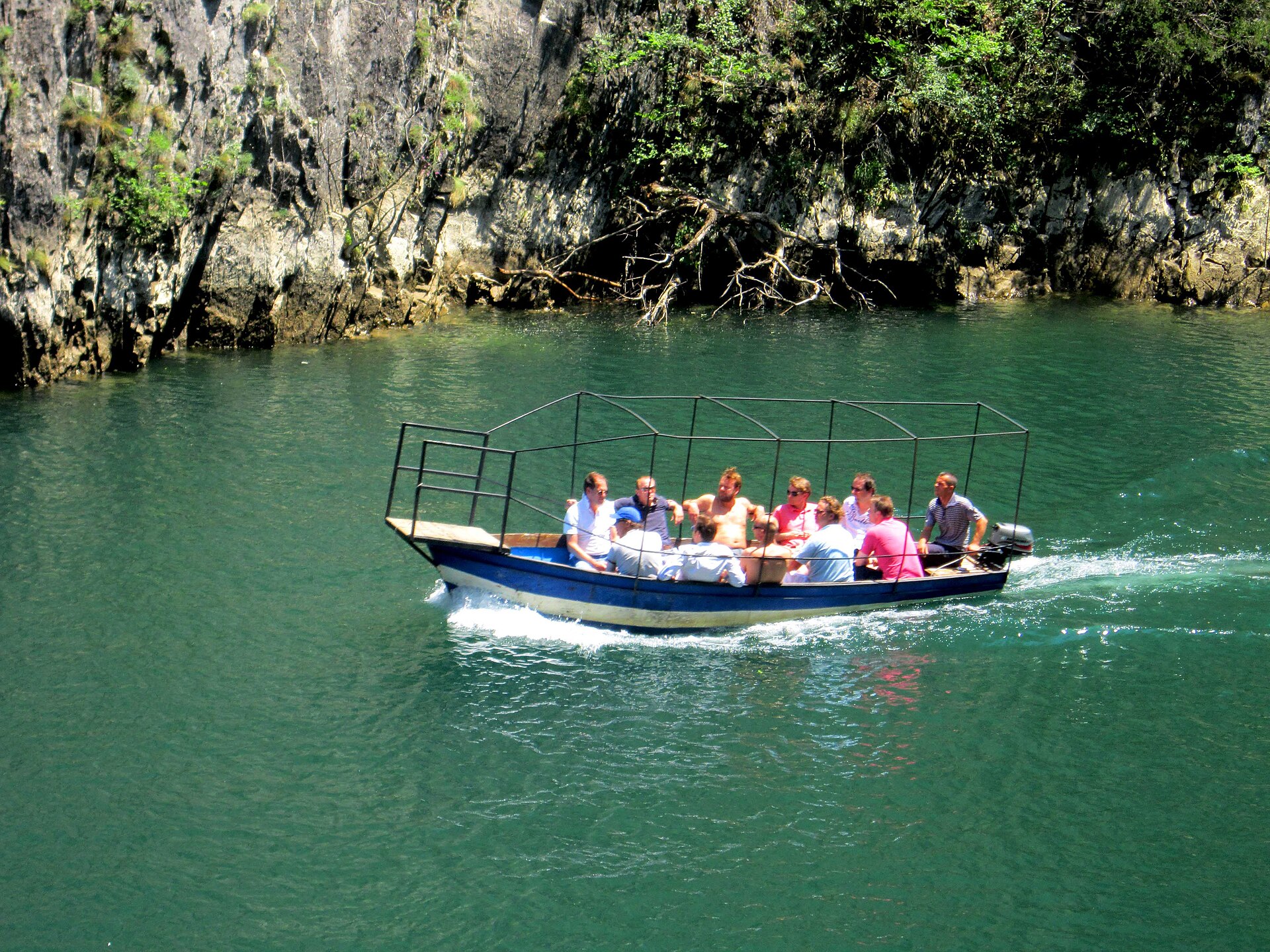 A tour boat cruising the green water of Lake Matka toward Vrelo Cave