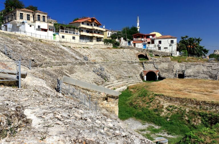 Ancient Roman amphitheater of Durres with stone seating and houses on its rim under a blue sky