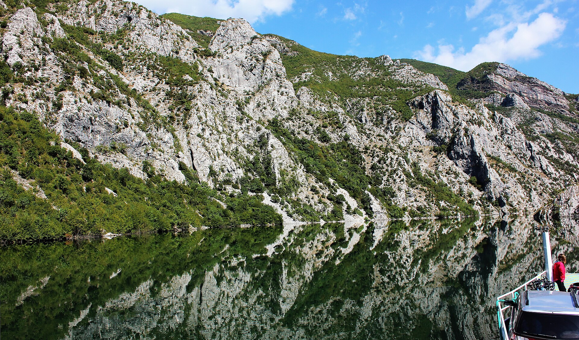 Komani Lake ferry reflected in green water between steep limestone cliffs in northern Albania