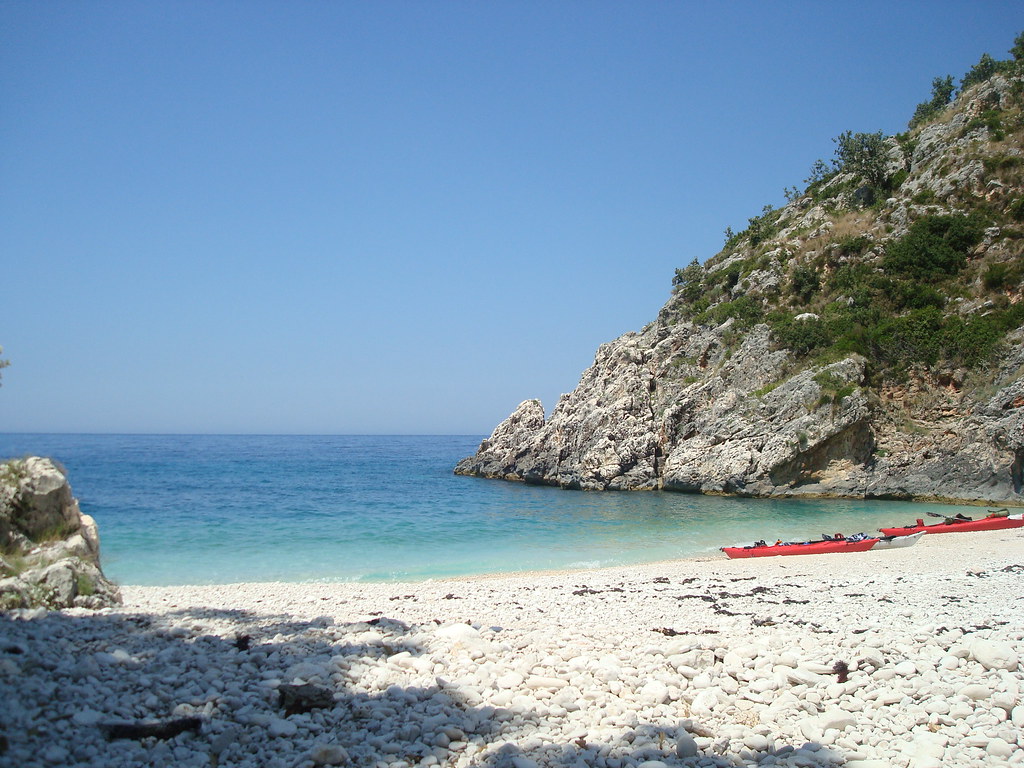 Kayaker on clear water beside a white pebble cove on the Albanian coast
