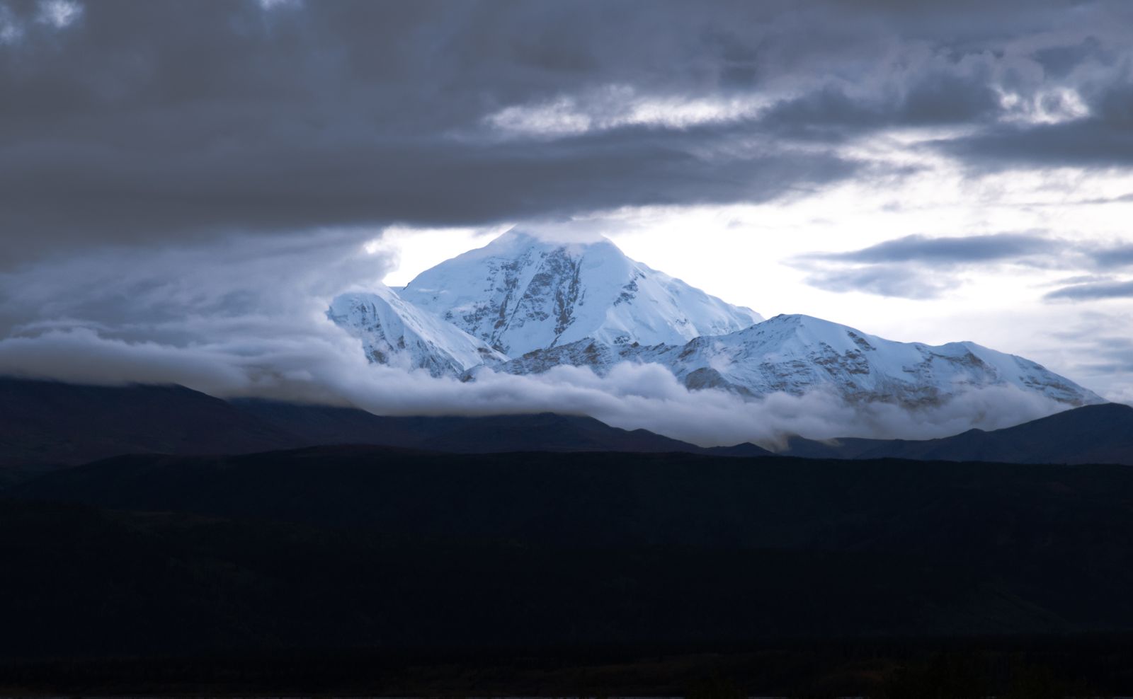 Snow-capped Denali peak with clouds parting above the Alaska wilderness