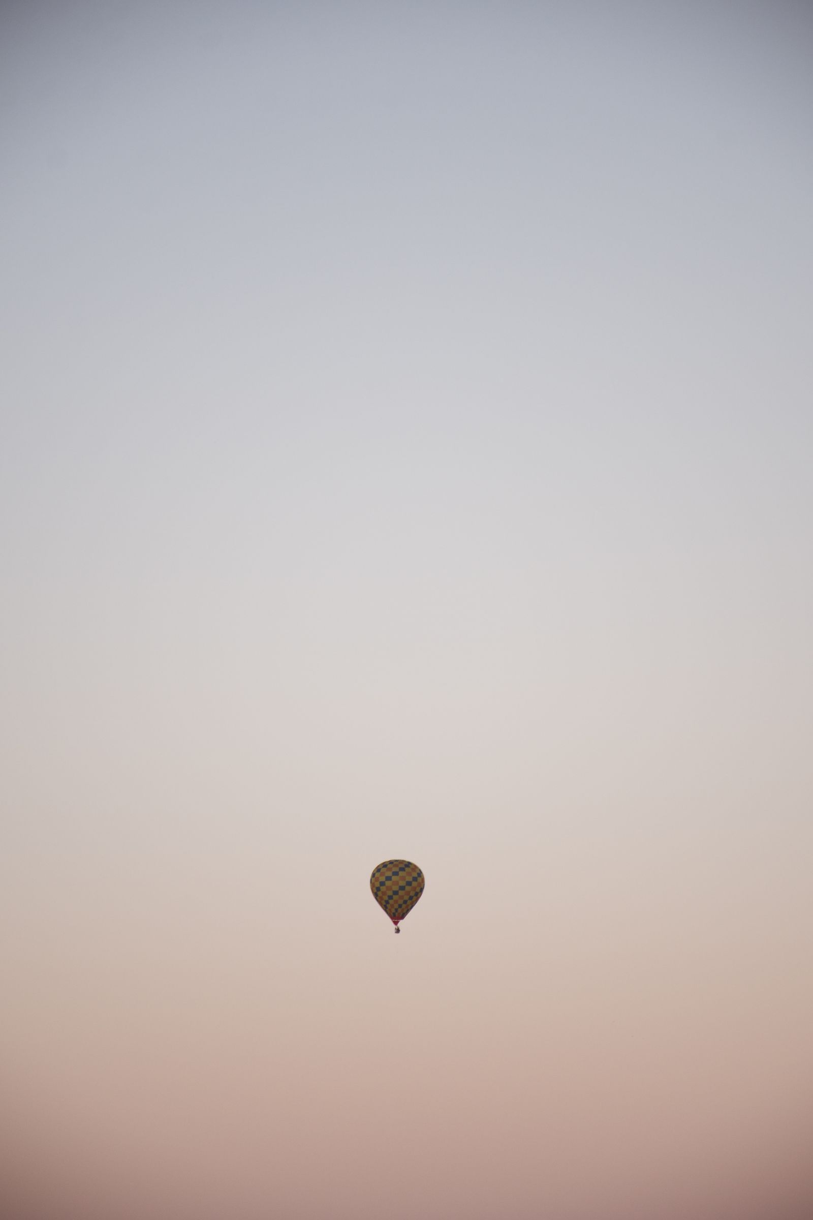 A single hot air balloon floating in a pink and blue sunrise sky over Albuquerque